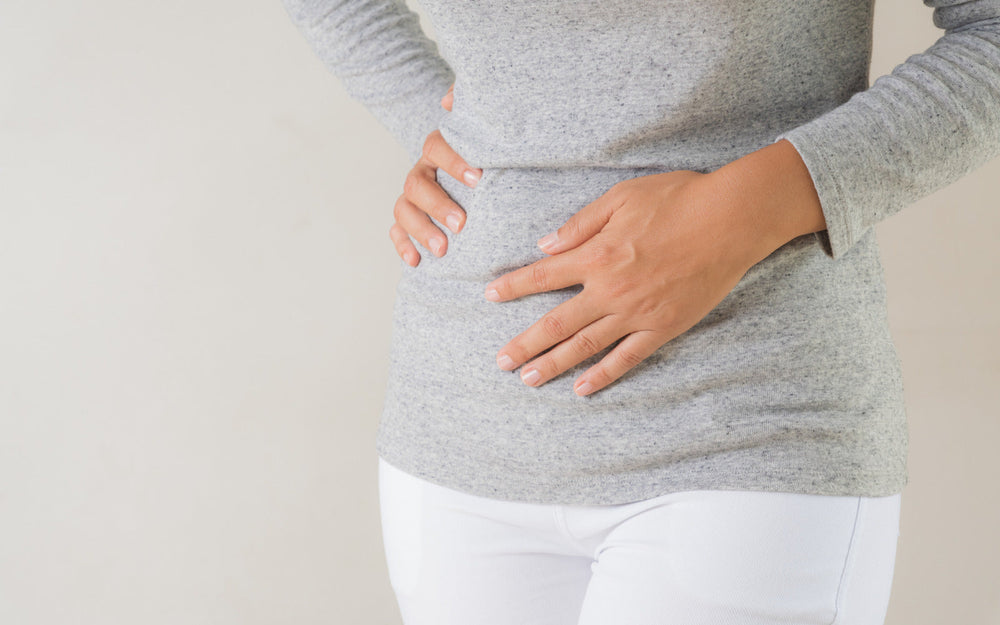 Woman holding her stomach, representing gas, bloating, and digestive discomfort often caused by gut imbalance.