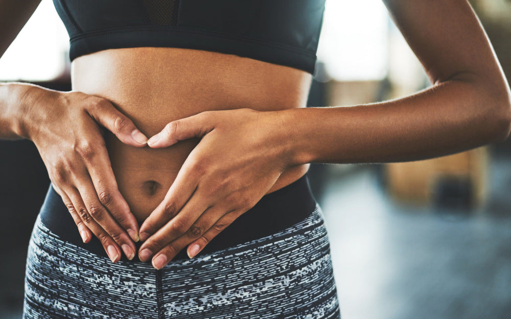 Woman in yoga clothing making a heart shape over her stomach, symbolizing gut health, balance, and overall wellness.