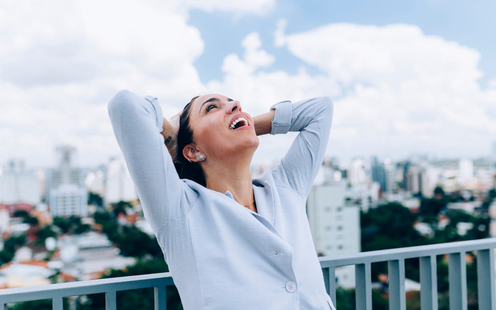 Smiling woman standing outside with hands behind her head, representing the feeling of relief and comfort after reducing bloating.