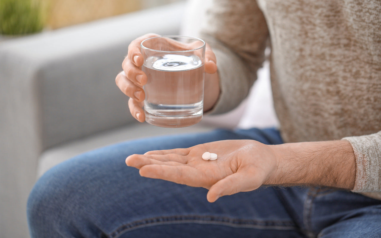 A man taking antibiotics with a glass of water, emphasizing the importance of gut health and probiotic support during antibiotic use.